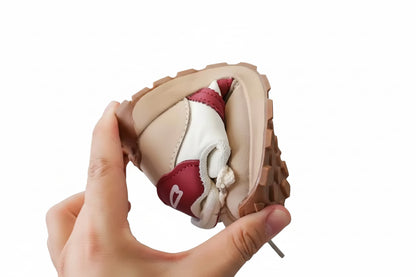 Baby shoe with brown and white design held by a hand against a blurred indoor background
