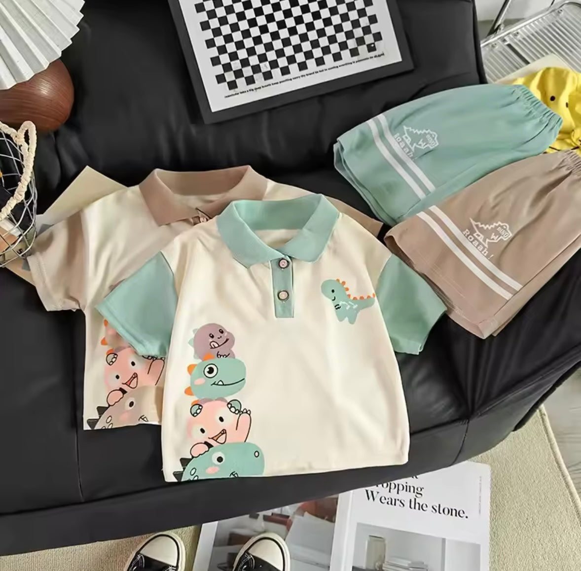Children's clothing with cartoon designs on a black leather couch.