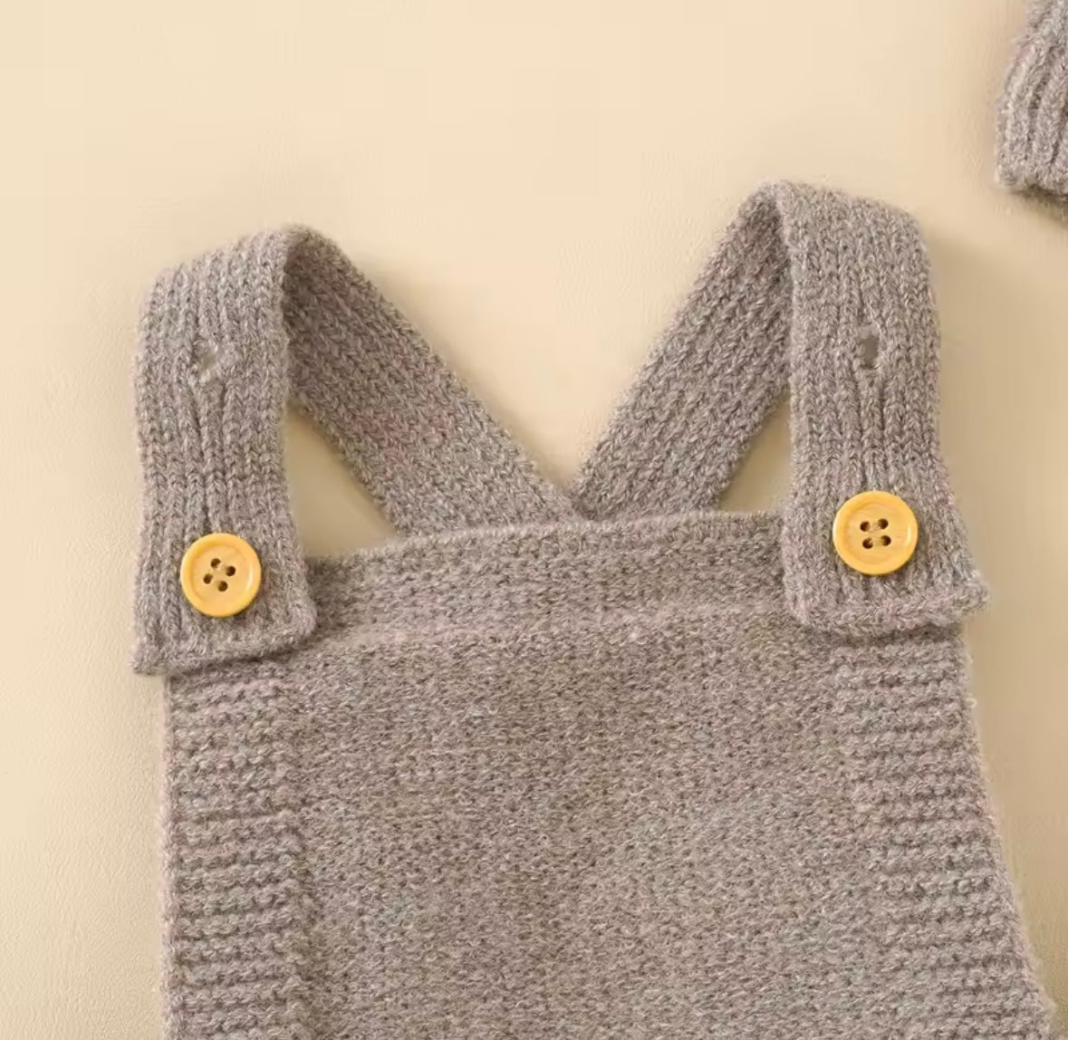 Gray knitted baby romper with wooden buttons on a beige background