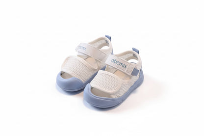 Pair of children's sandals with 'abcmix' branding on a chair.