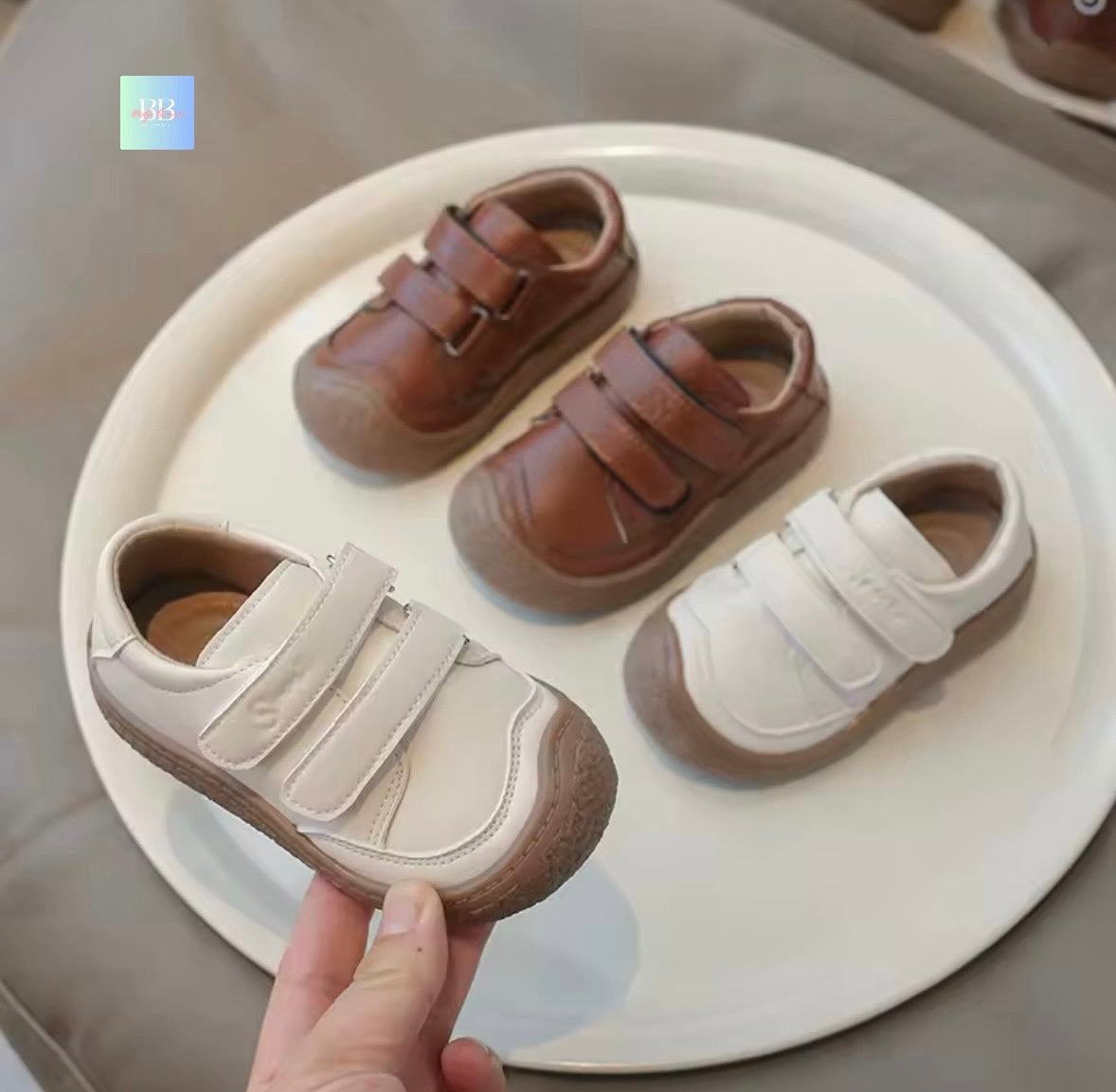 Pair of brown and beige children's shoes on a white plate with a hand holding one shoe.