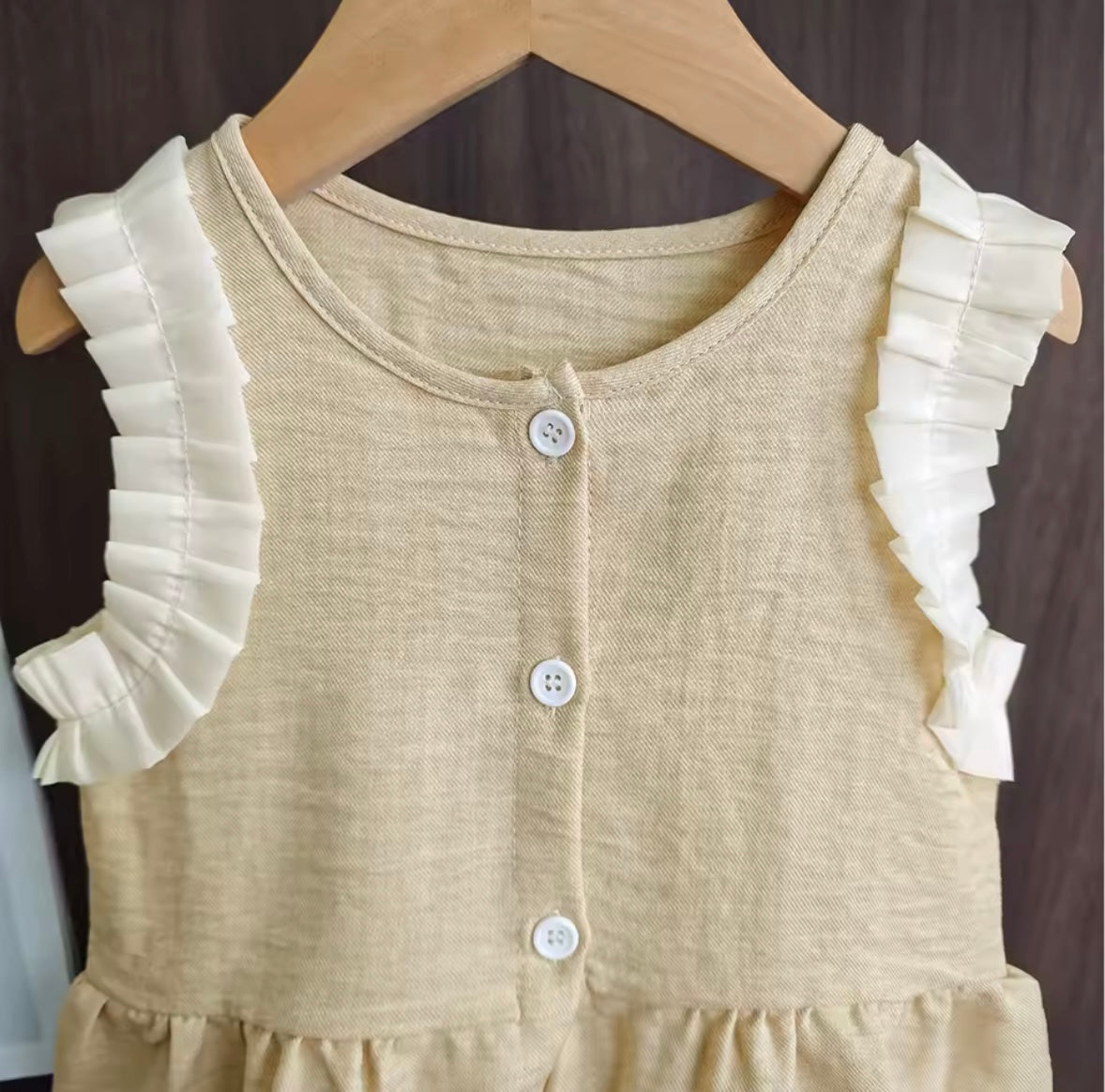 Beige dress with white ruffled sleeves on a wooden hanger against a dark background