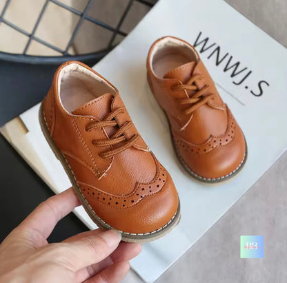 Brown leather shoes on a white surface with a hand holding one shoe.