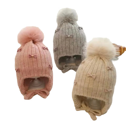 Three knitted hats with pom-poms and bow details on a soft white background