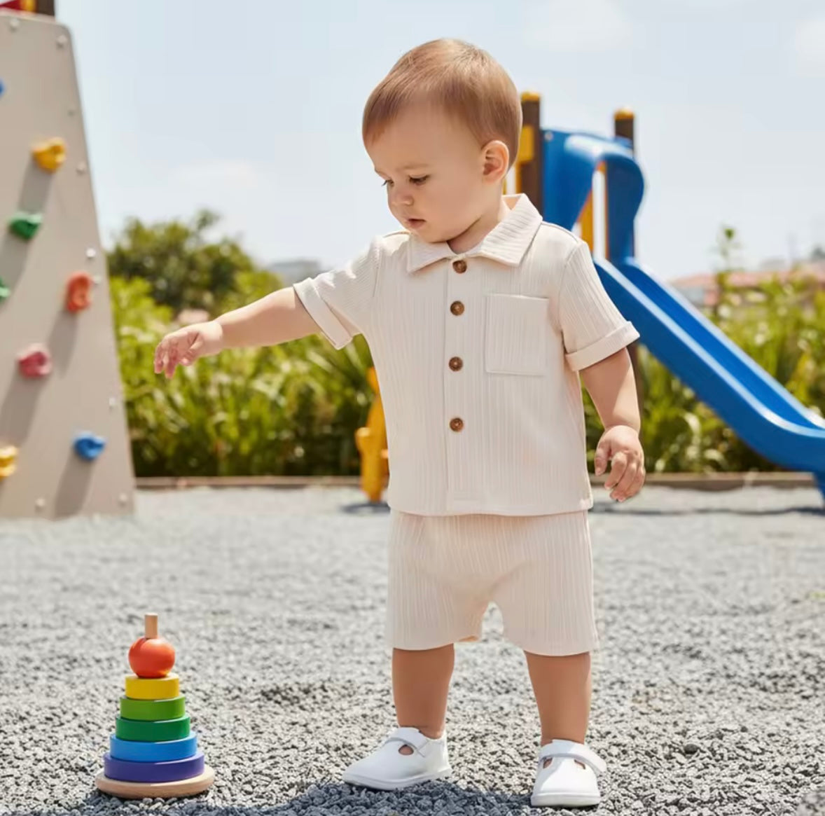 Child in a beige outfit standing on a playground with a colorful toy stack.