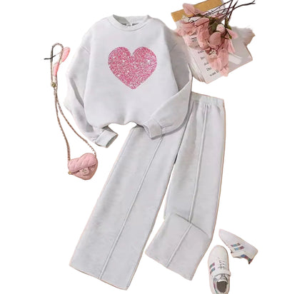 White sweatshirt with pink heart design and gray pants on a wooden surface.
