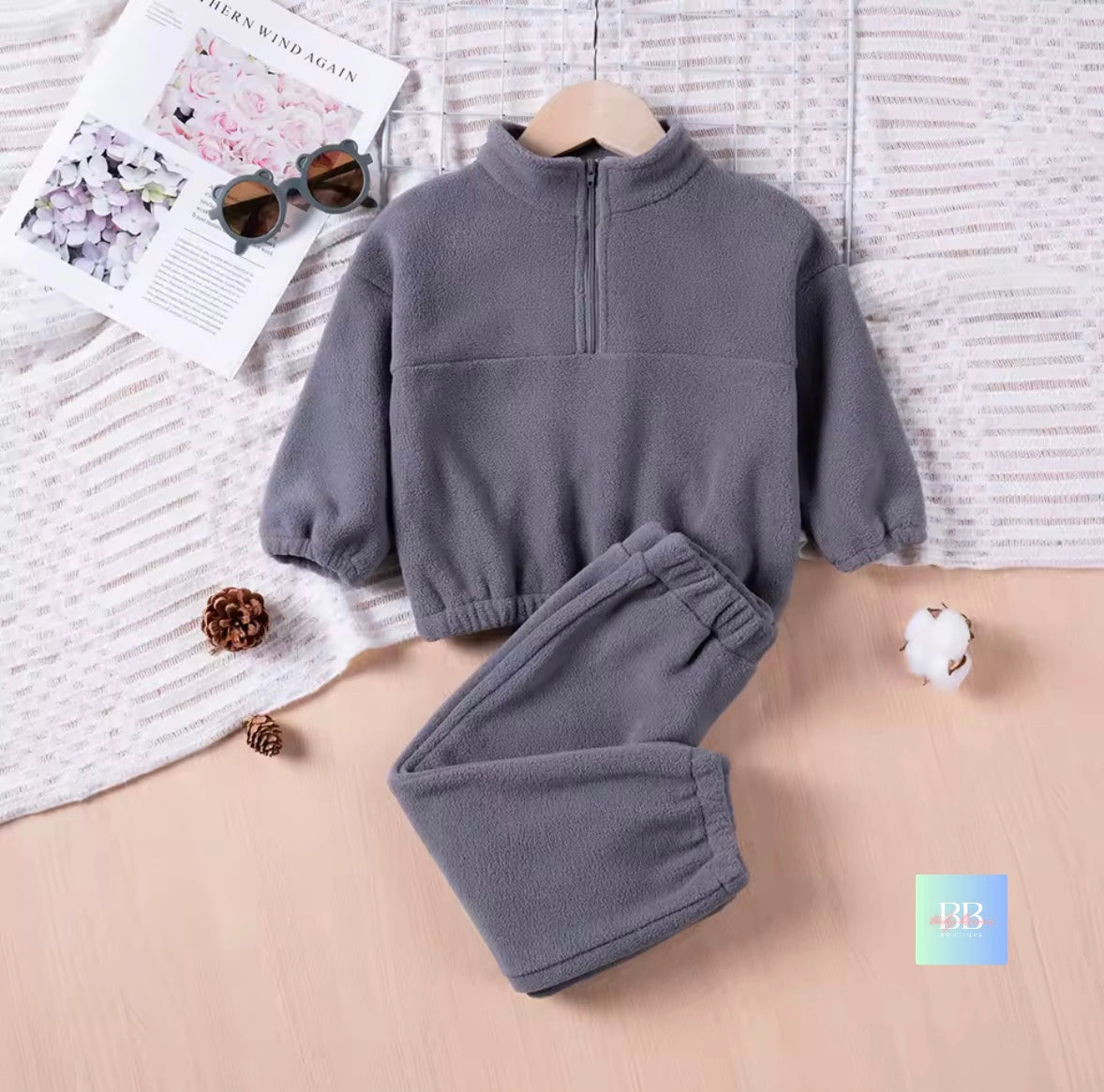Gray fleece set with pants on a textured surface with a magazine and sunglasses.