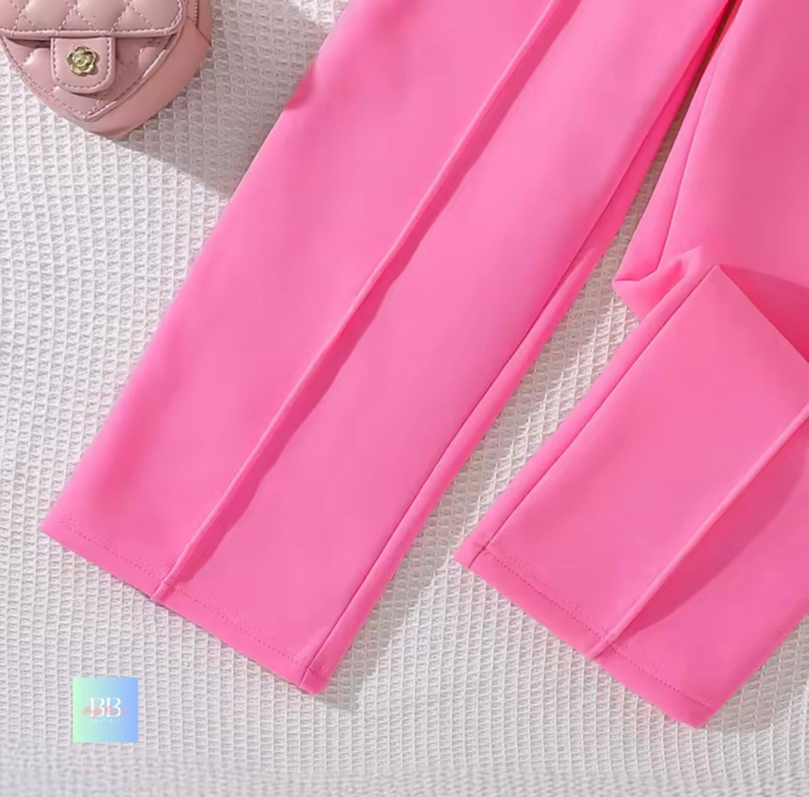 Close-up of pink pants on a textured white surface with a small pink bag in the corner.