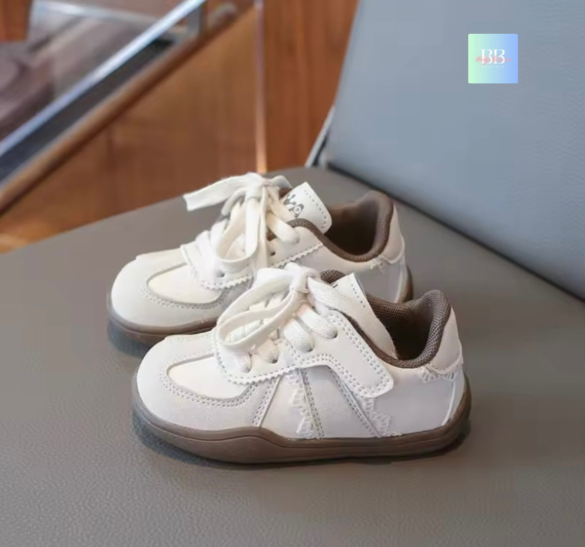 Pair of white sneakers with brown soles on a gray surface.