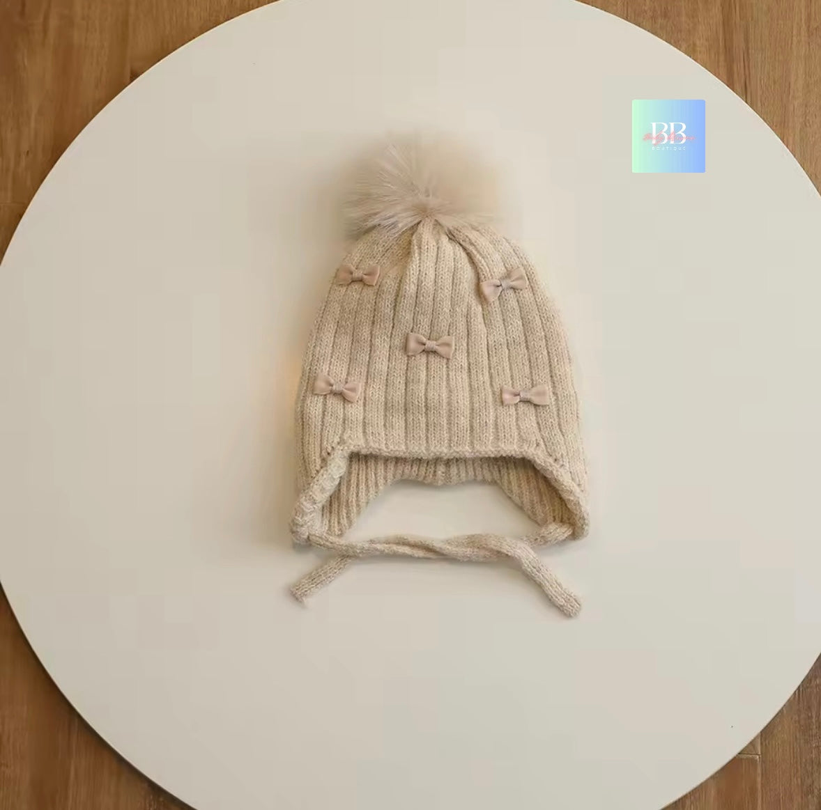 Knitted baby hat with earflaps and bow details on a white surface.