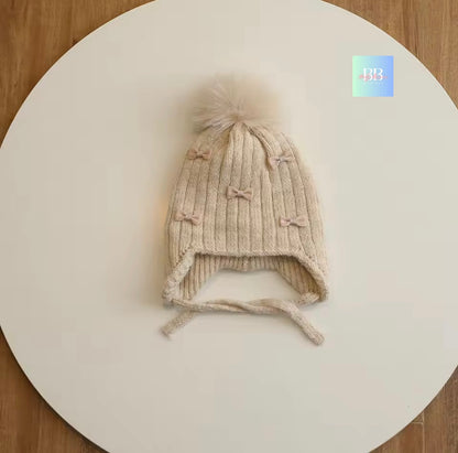 Knitted baby hat with earflaps and bow details on a white surface.