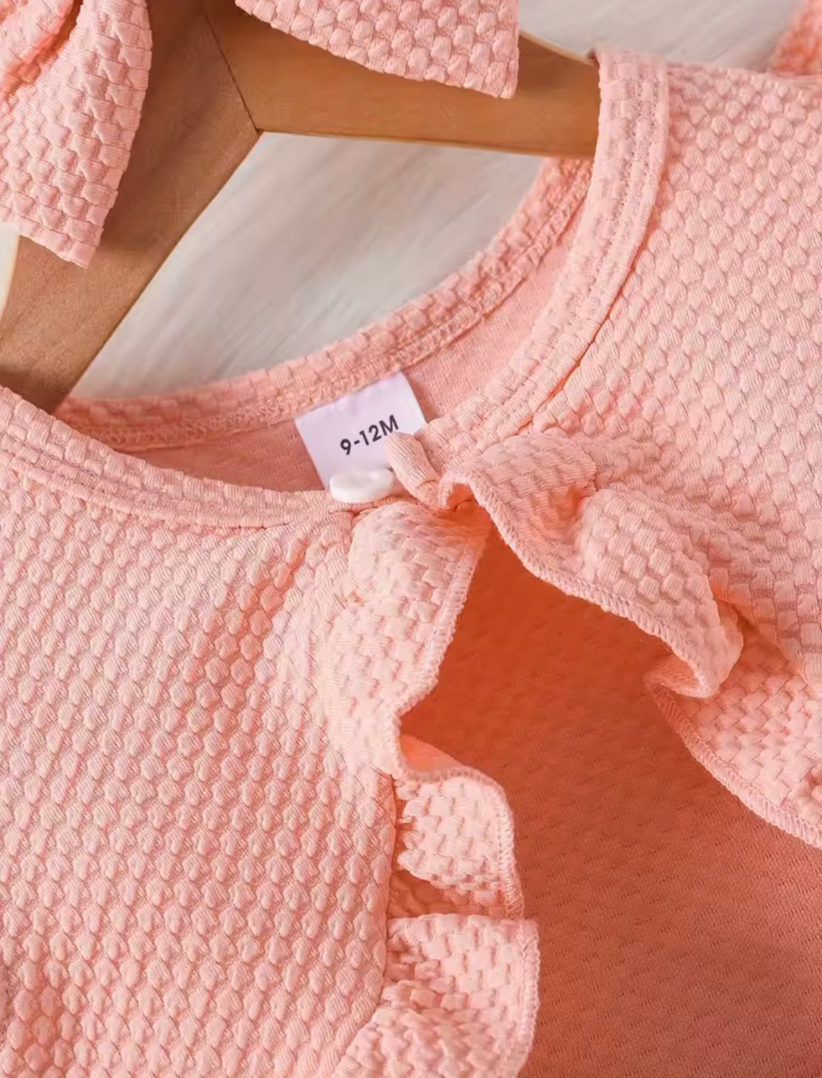 Close-up of a pink textured garment with a size tag on a light wooden surface.