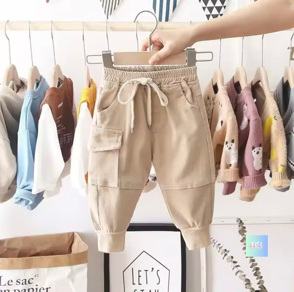 Beige children's pants hanging on a rack with other colorful clothes in the background.