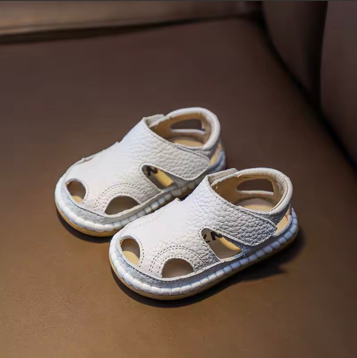 Pair of white children's sandals on a brown surface