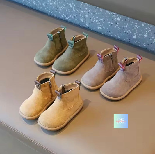Three pairs of children's boots in green, beige, and brown on a gray surface.