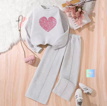 White sweatshirt with pink heart design and gray pants on a wooden surface.
