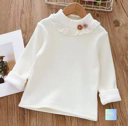 White long-sleeve shirt with floral details on a wooden surface