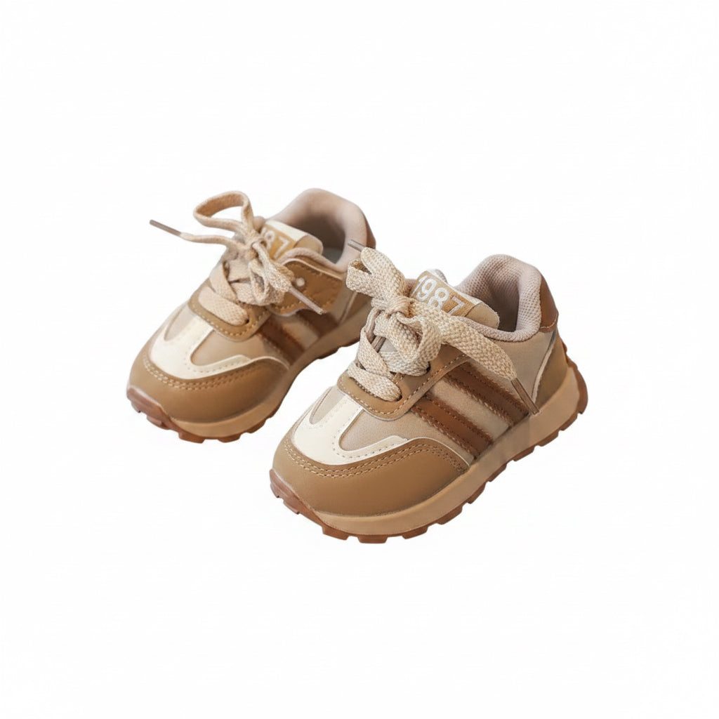 Beige children's sneakers held by a hand on a reflective surface