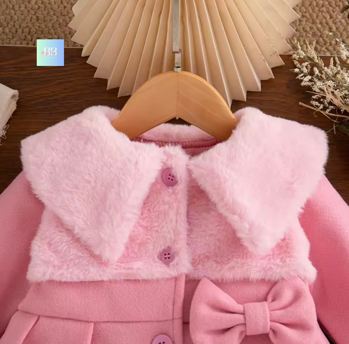 Pink children's coat with fluffy collar on a wooden hanger against a neutral background