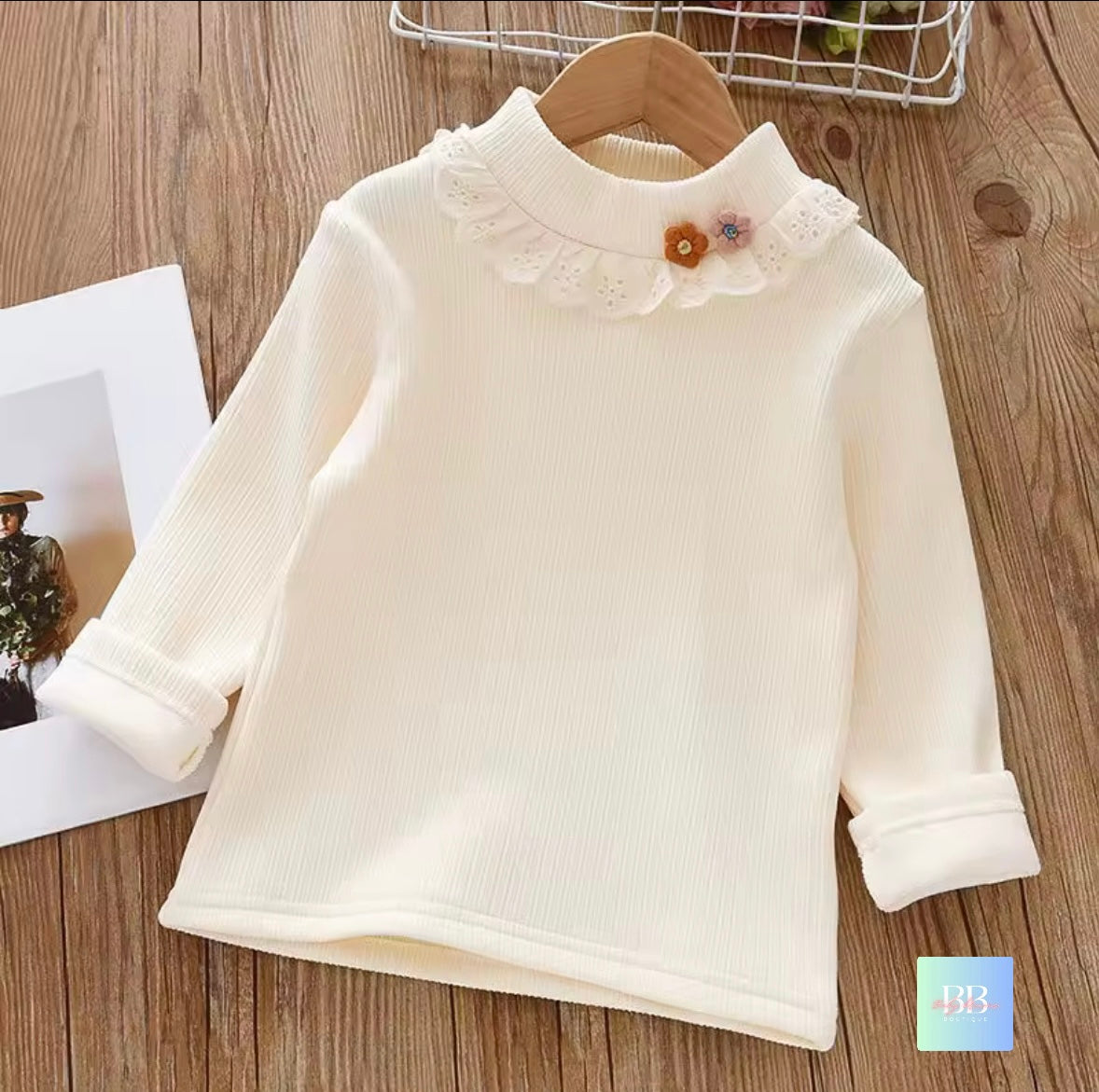 White long-sleeve shirt with floral details on a wooden surface