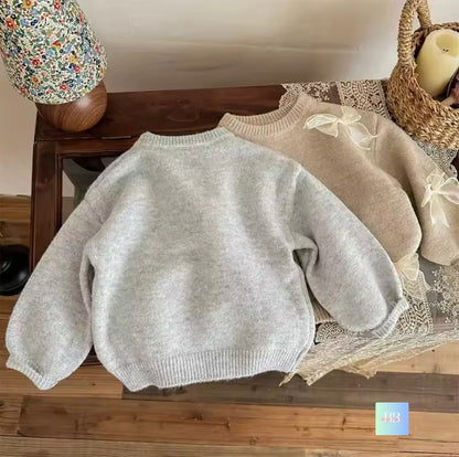 Two sweaters, one gray and one beige with lace details, on a wooden surface.
