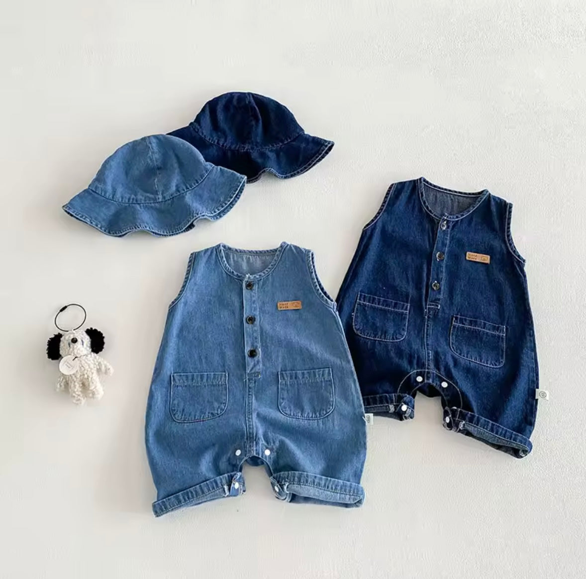 Two denim rompers and a matching hat on a light gray background