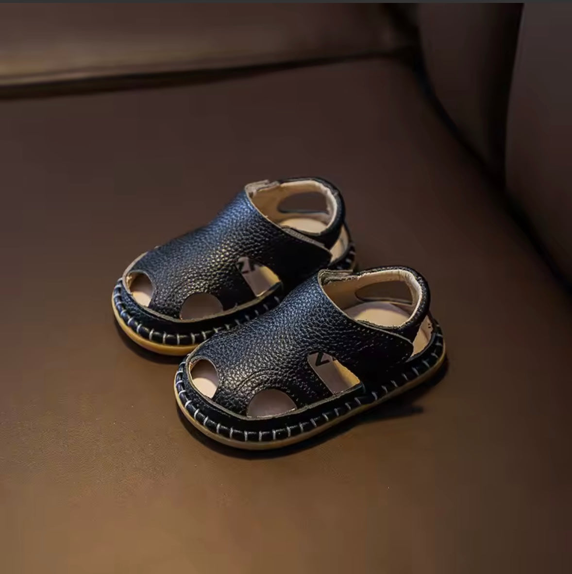 Pair of black children's sandals on a brown surface