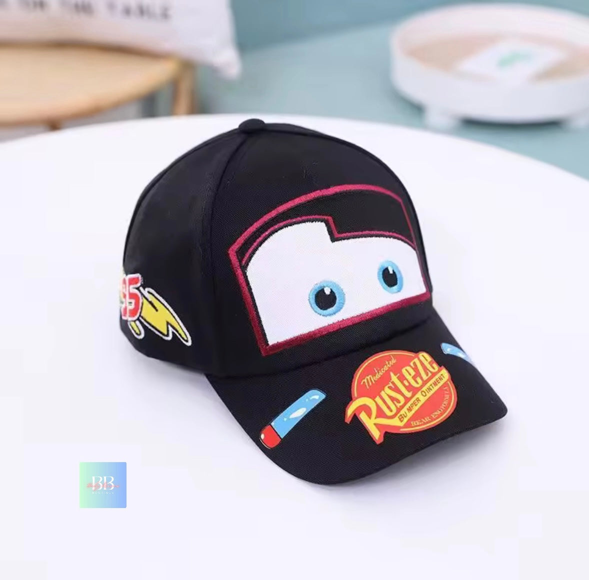 Black cap with cartoon face design and colorful patches on a white surface.