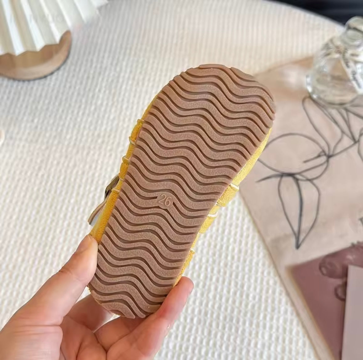 Close-up of a shoe sole with wavy pattern held by a hand on a textured surface.