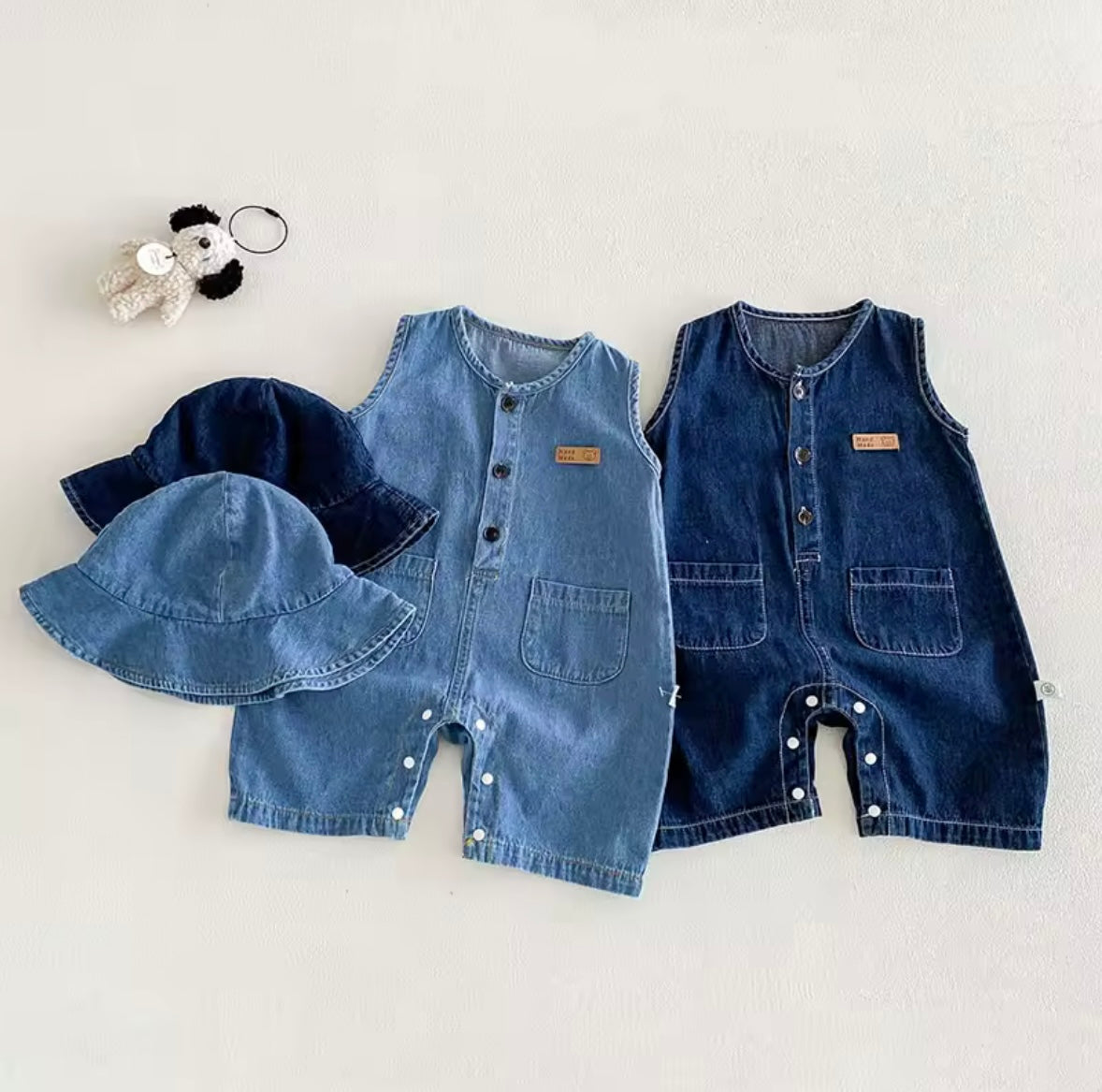 Two denim baby rompers and a hat on a light gray background