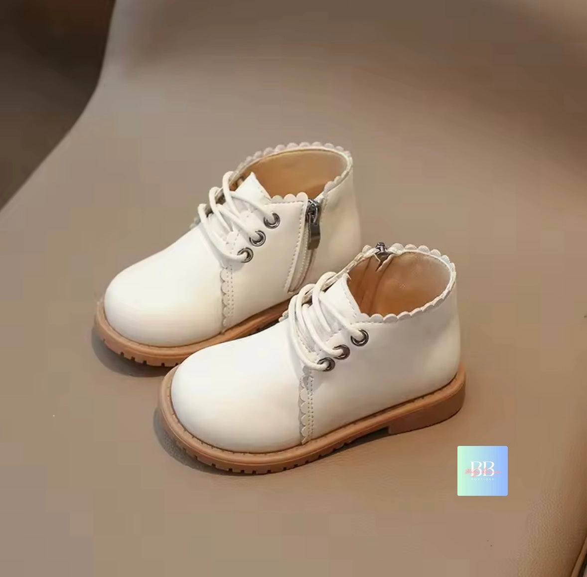 Pair of white children's boots with brown soles on a beige surface