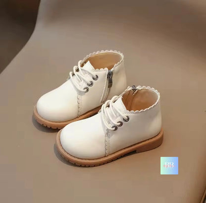 Pair of white children's boots with brown soles on a beige surface