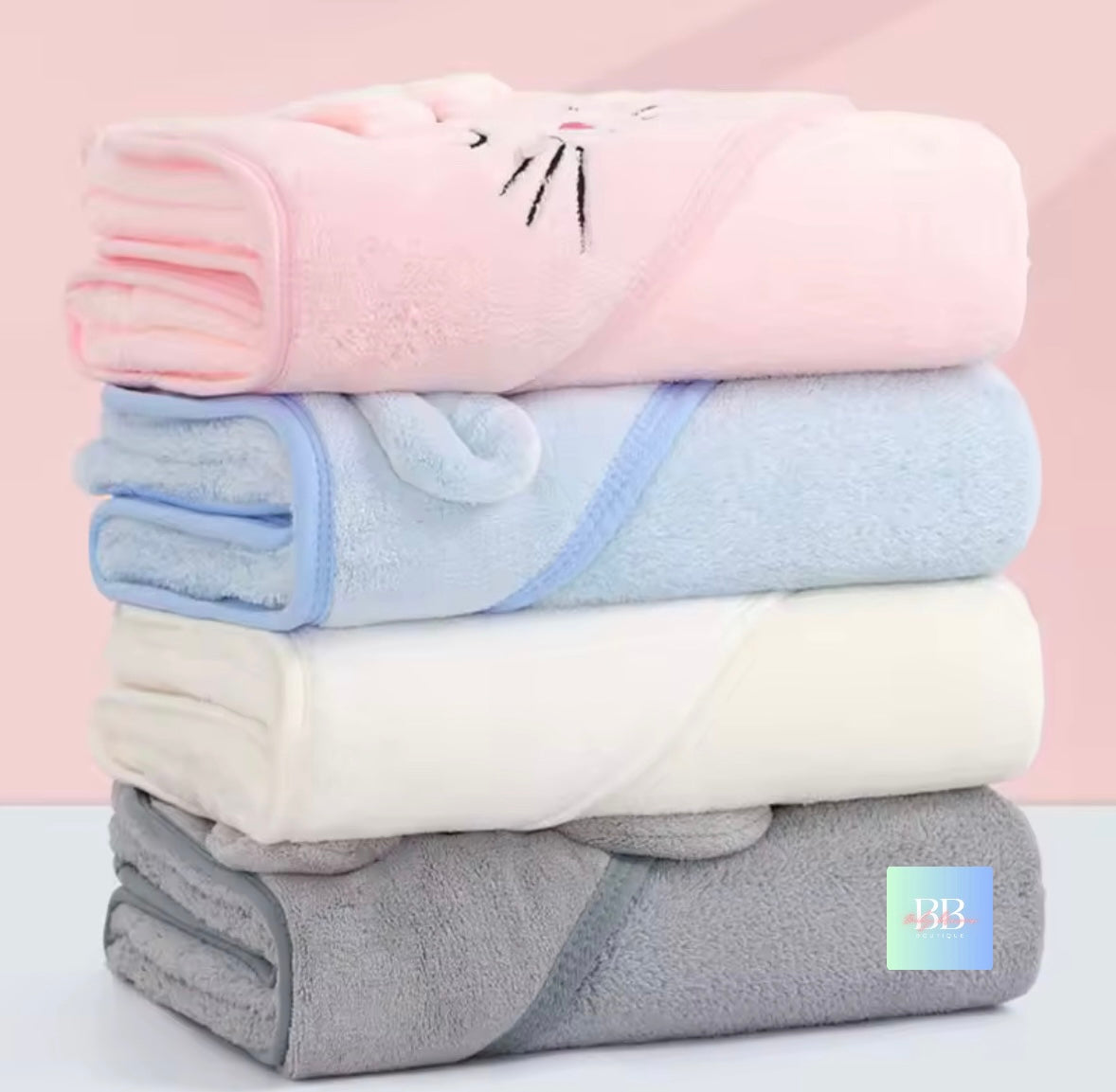 Stack of folded blankets in pink, blue, white, and gray on a light pink background