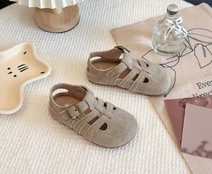 Pair of beige sandals on a textured surface with a bottle and decorative items.