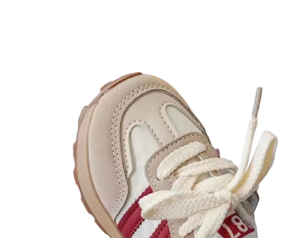 Close-up of a beige and red sneaker with white laces on a blurred background