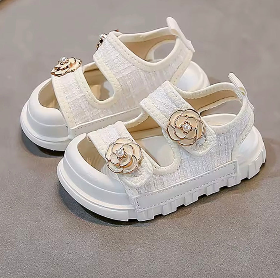 White children's sandals with floral embellishments on a gray surface