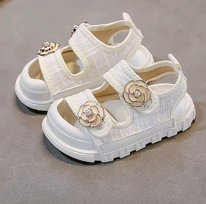 White children's sandals with floral embellishments on a gray surface