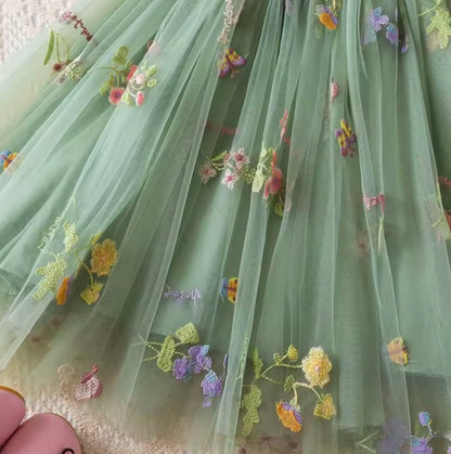 Green fabric with floral embroidery held by a hand
