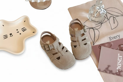 Pair of beige sandals on a textured surface with a bottle and decorative items.