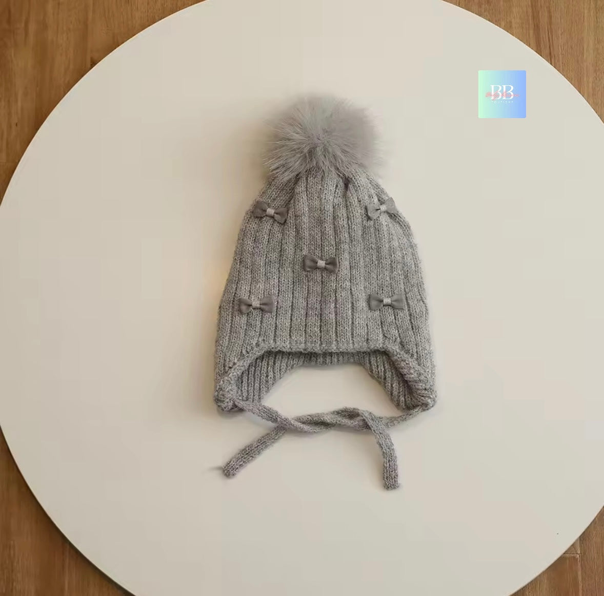 Gray knit baby hat with a pom-pom on a white surface