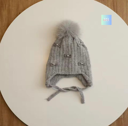 Gray knit baby hat with a pom-pom on a white surface