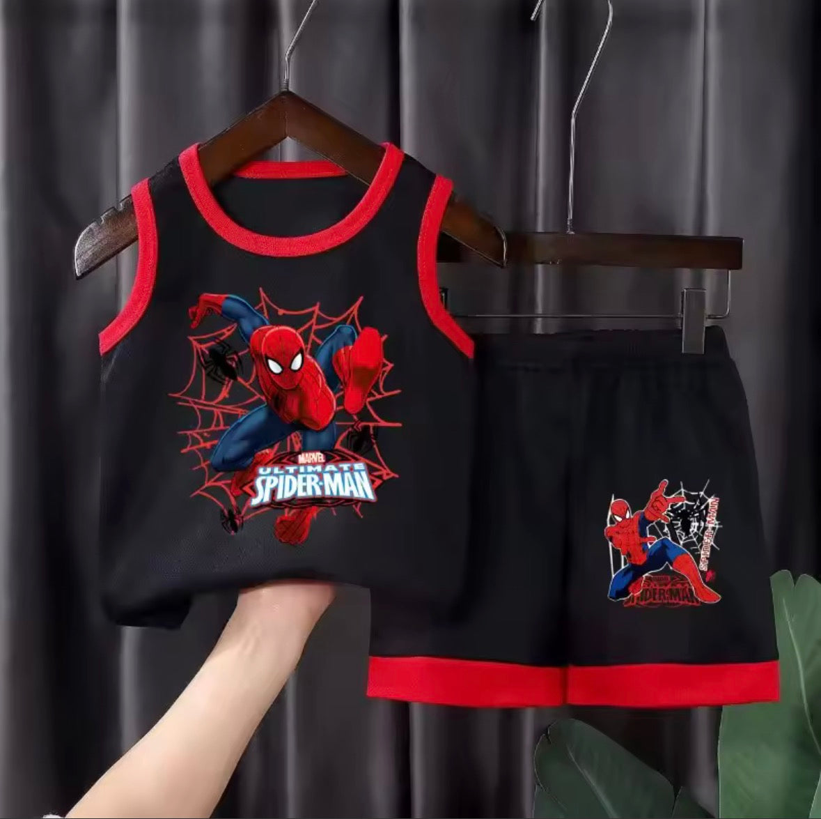 Black tank top and shorts set with Spider-Man design on a hanger against a dark curtain background.