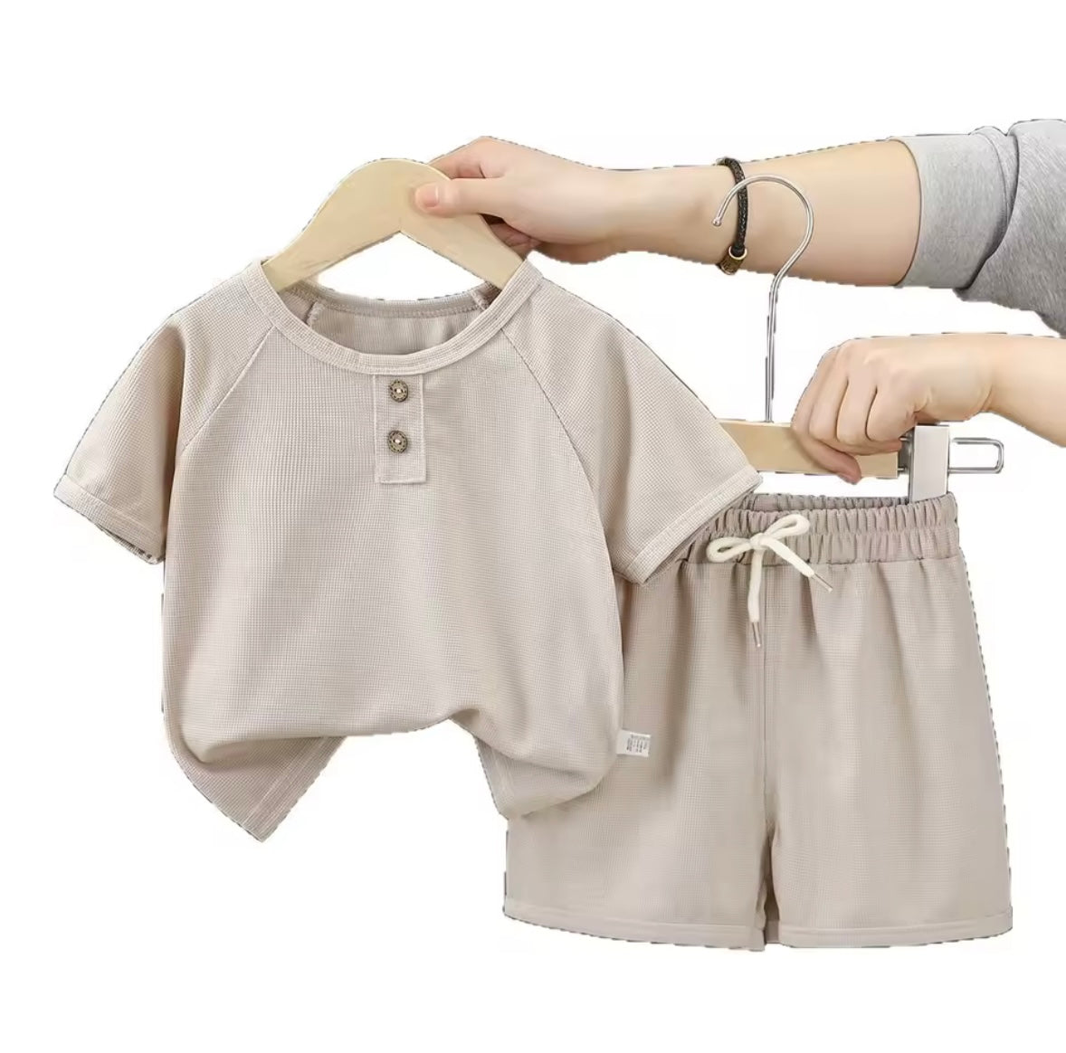 Beige baby outfit with shirt and shorts on hangers against a white background