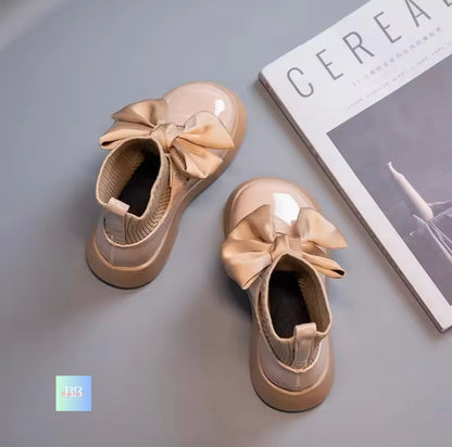 Pair of beige shoes with large bows on a gray surface next to a magazine.