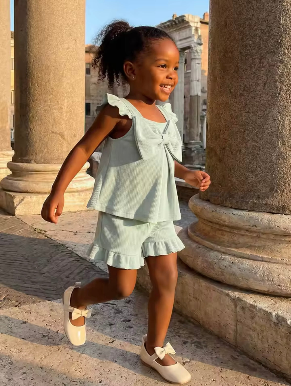 Young girl in a light green outfit running between stone columns.