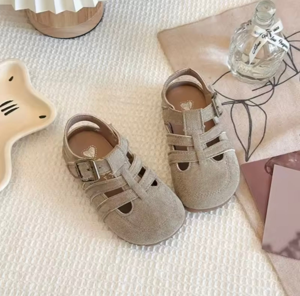 Pair of gray sandals on a textured surface with a bottle and decorative items.