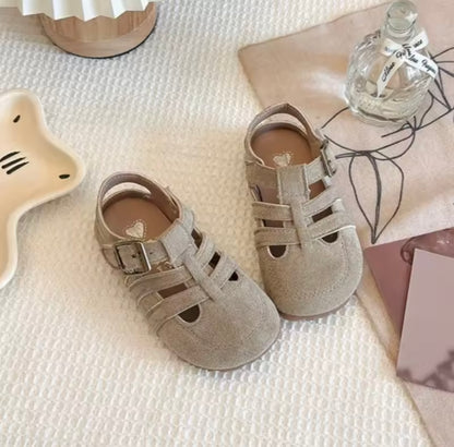 Pair of gray sandals on a textured surface with a bottle and decorative items.