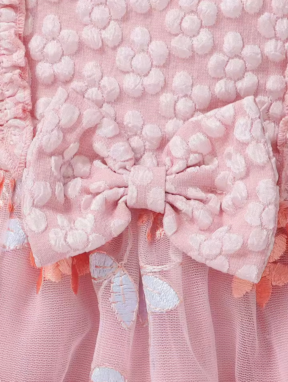 Close-up of a pink textured fabric with a bow and floral details