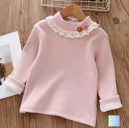 Pink children's sweater with lace collar on a wooden surface
