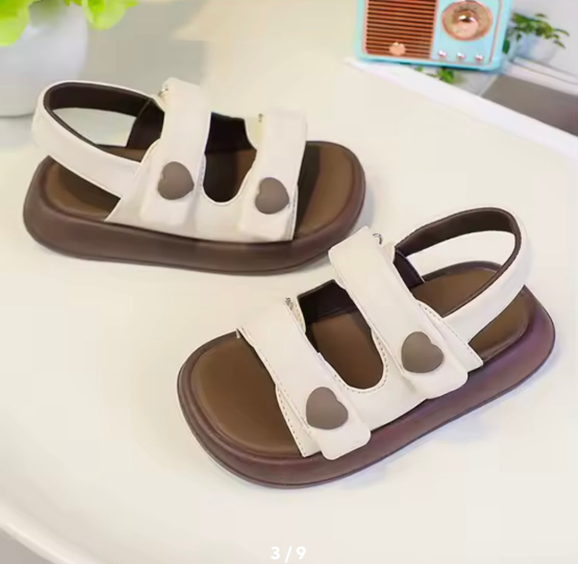 Pair of white sandals with brown soles on a white surface.